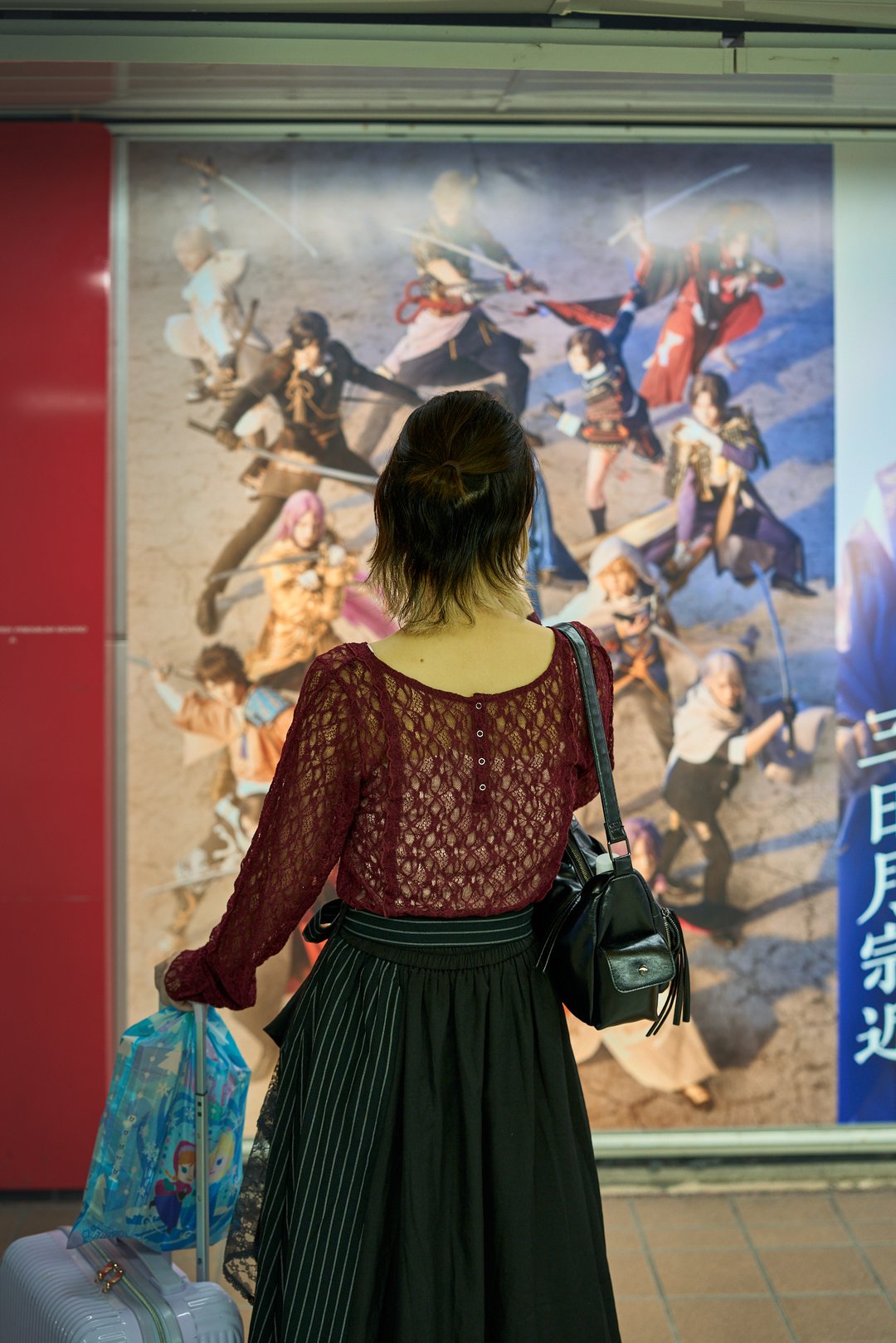 Pictured is a person back, looking at a cool posters of an anime of sort
